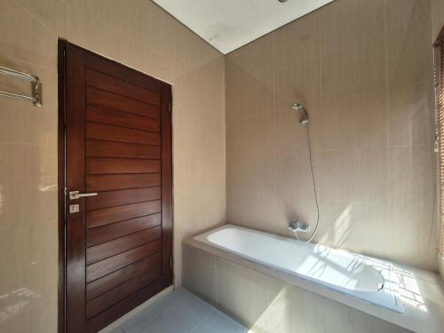 a bathroom with a bath tub and a wooden door at The Bagus in Kerobokan