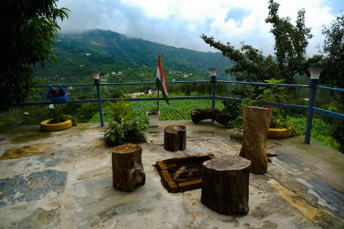a patio with logs and a fire pit with mountains in the background at Saanidhya Homestay in Mukteswar