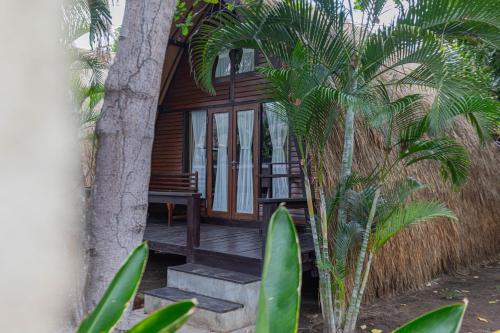 a house with a wooden porch with palm trees at Omah Gili Hotel in Gili Air