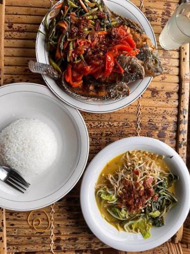 three plates of food on a wooden table with rice at Jonny's Places in Tetebatu
