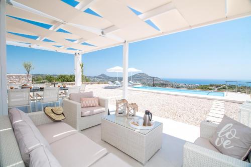 a patio with white furniture and a view of the ocean at Francis & Gregorys Luxury Villas in Afantou