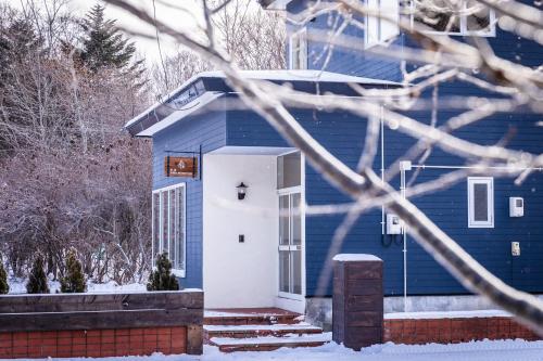 a blue house with a white door in the snow at ヴィラYukara緑屋 in Nanae