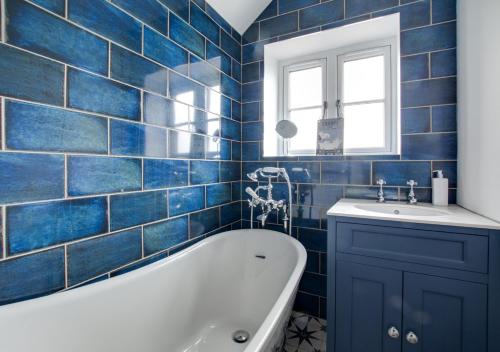 a blue tiled bathroom with a tub and a sink at Warborough House East in Kelling