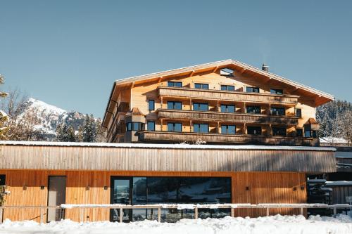 a large wooden building with snow in front of it at Alpenhotel Kitzbühel am Schwarzsee - 4 Sterne Superior in Kitzbühel