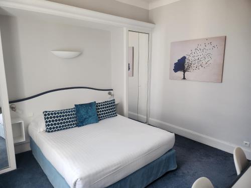 a small bedroom with a white bed with blue pillows at Hôtel Les Nations The Originals Boutique VICHY in Vichy
