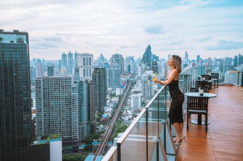 a woman standing on the edge of a balcony with a drink at Bangkok Marriott Hotel Sukhumvit in Bangkok