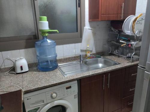 a kitchen counter with a washing machine and a bottle of water at Lovely 2Bhk Family Apartment in Ajman in Al Ḩamīdīyah