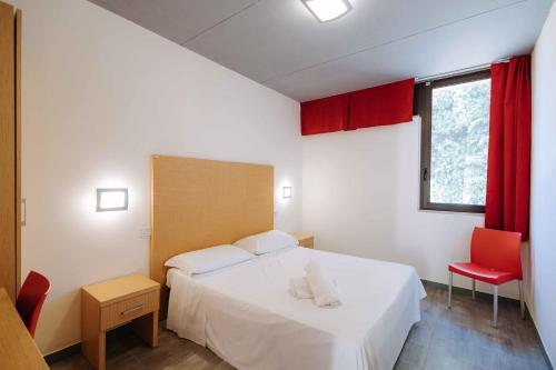 - une chambre avec un lit blanc et une chaise rouge dans l'établissement Nicolaus Club Magna Grecia, à Métaponte