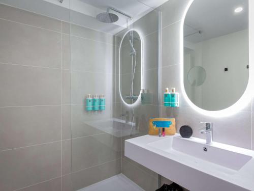 La salle de bains blanche est pourvue d'un lavabo et d'un miroir. dans l'établissement Novotel Aix-en-Provence Pont de L'Arc, à Aix-en-Provence