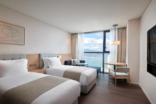 two beds in a hotel room with a view of the ocean at Shilla Stay Yeosu in Yeosu