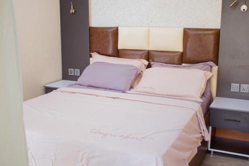 un grand lit avec des draps blancs et une tête de lit marron dans l'établissement Stay Apartment, à Kigali