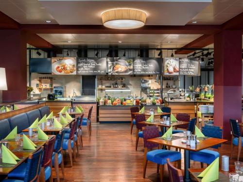 une salle à manger avec des tables et des chaises ainsi qu'un restaurant dans l'établissement Mövenpick Hotel Nürnberg Airport, à Nuremberg