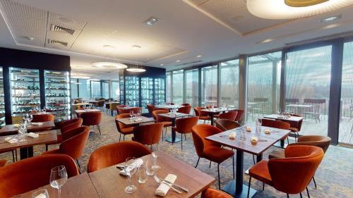 un restaurante con mesas, sillas y ventanas en DoubleTree by Hilton Lyon Eurexpo, en Saint-Priest