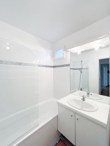 La salle de bains blanche est pourvue d'un lavabo et d'une baignoire. dans l'établissement La Douce Évasion à 13 minutes du château de Versailles, à Saint-Cyr-lʼÉcole