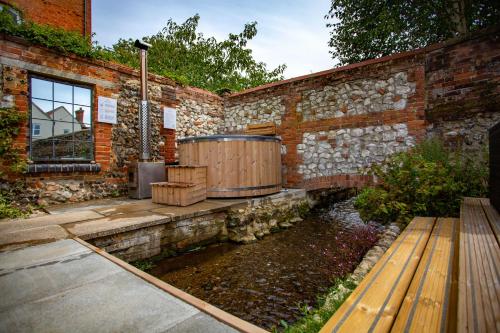 uma banheira de hidromassagem ao lado de uma parede de tijolos com um banco de madeira em The Old Chequers em Fakenham