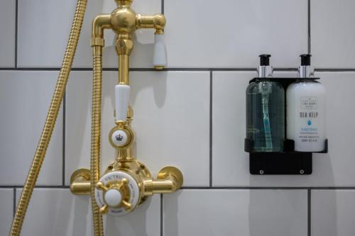 a gold shower faucet with a bottle of shampoo at Queen Charlotte Guesthouse in Edinburgh