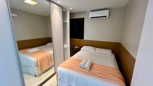 um pequeno quarto com 2 camas e um espelho em EDF SEVILHA - Apartamento com 1 suíte climatizada e 2 Banheiros, Sala Climatizada a 300 metros da Beira-Mar de Ponta Verde - EXCELENTE LOCALIZAÇÃO em Maceió
