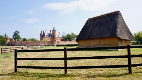 a thatch roofed house in a field with a fence at Château de Tilly in Boissey-le-Châtel