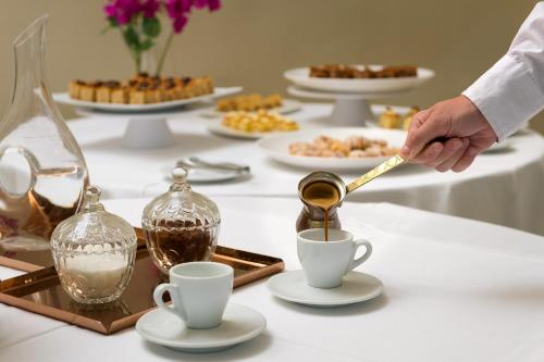 a person pouring coffee into cups on a table at Lindos Village Resort & Spa - Adults Only in Líndos