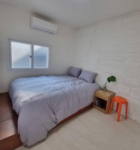 a white bedroom with a large bed and a orange stool at Studio Sum in Seoul