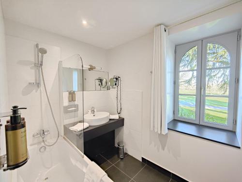 a white bathroom with a sink and a window at Hotel Château de la Barbinière in Saint-Laurent-sur-Sèvre