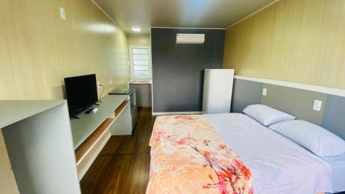 um pequeno quarto com uma cama e uma televisão em Kitinete Mobiliada em Chapecó