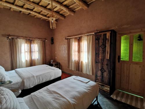 a bedroom with two beds and two windows at Maison d'hôte tamatart - Homestay in Kalaat MGouna