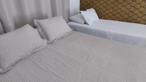 Duas camas com lençóis brancos e almofadas num quarto em Suíte Studio 2 Enseada Tortuga Mobiliada no Guarujá