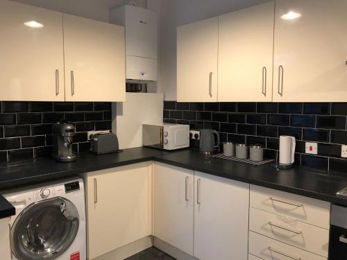 a kitchen with white cabinets and a washing machine at Comfortable Home From Home Bolton Central - Sleeps - 10 in Bolton