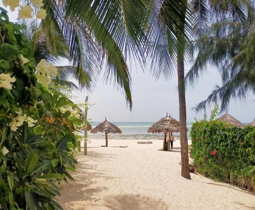 a beach with straw umbrellas and the ocean at Pole Pole Beach House in Watamu