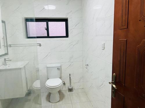 La salle de bains blanche est pourvue de toilettes et d'une fenêtre. dans l'établissement Roma Apartments, à Lusaka