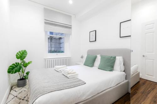 a white bedroom with a bed and a plant at Luxury Apartments - Fitzrovia in London