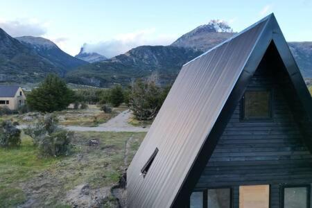 a house with a roof with mountains in the background at OUTSCAPE l Cabaña Familiar en mejor sector de Cerro Castillo in Villa Cerro Castillo
