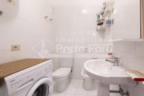 baño blanco con lavadora y lavamanos en 9C - Bilocale con spaziosa terrazza sul mare Porto Mannu, en Palau