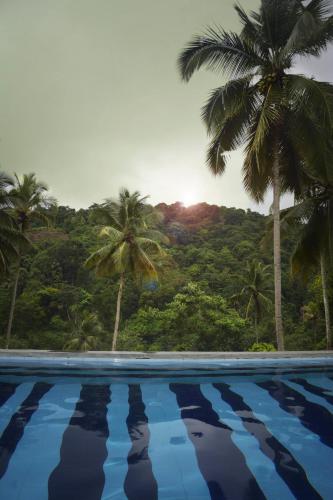 a swimming pool with palm trees in the background at Athulya Villas, Kandy in Kadugannawa