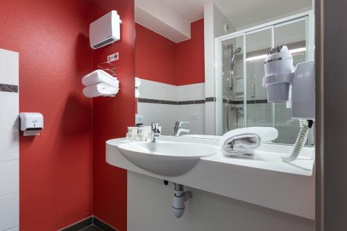 La salle de bains est pourvue d'un lavabo blanc et de murs rouges. dans l'établissement Ace Hôtel Paris Marne La Vallée, à Bailly-Romainvilliers