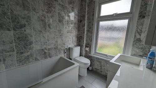 a bathroom with a tub and a toilet and a window at 3 bedroom house,4beds, 2 baths Ilford ,12 mins to Stratford in London