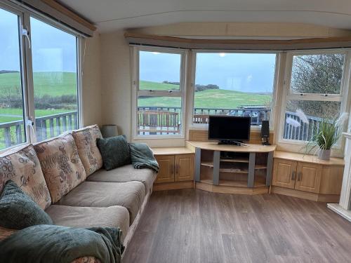 een woonkamer met een bank, een tv en ramen bij Captivating 2-Bed static caravan in Holyhead in Llanfachraeth