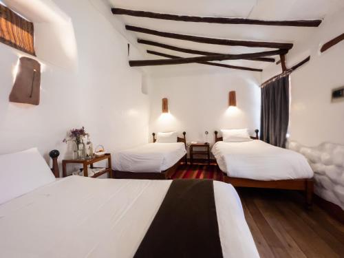 two beds in a room with white walls and wooden floors at El Balcón in Cusco