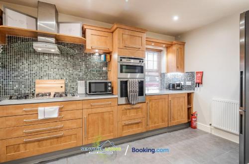 a large kitchen with wooden cabinets and appliances at Pet Friendly Spacious Townhouse By Sentinel Living Short Lets & Serviced Accommodation Windsor Ascot Maidenhead With Free Parking in Winkfield