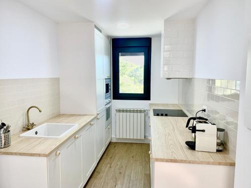 a white kitchen with a sink and a window at CHALET NUEVO EN LA MONTAÑA, CON CHIMENEA in Torremocha de Jarama