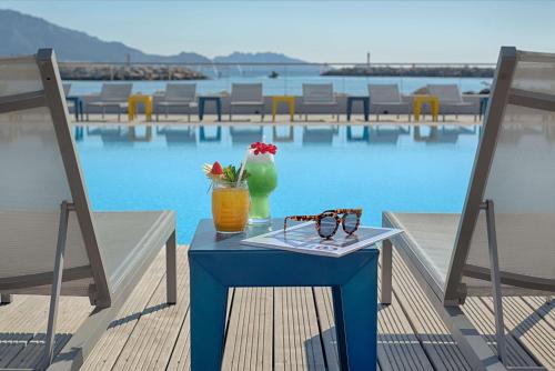 una mesa azul con una bebida y copas en la parte superior de una piscina en nhow Marseille en Marsella