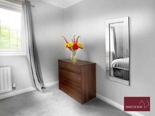 a vase of flowers on a dresser in a room with a mirror at Knaphill - 2 Bed House - Private Garden & Parking in Brookwood