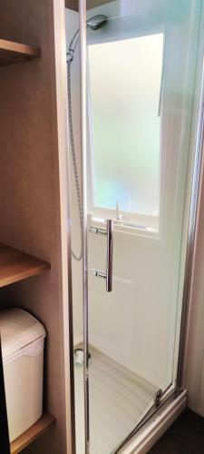 La salle de bains est pourvue d'une porte de douche en verre et d'une fenêtre. dans l'établissement Bungalow à Onzain avec piscine partagée et jardin, à Onzain