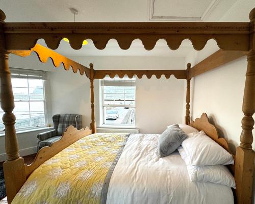 a bedroom with a canopy bed with a chair and a window at Historic 'Old Toll House' Shaldon Bridge in Teignmouth