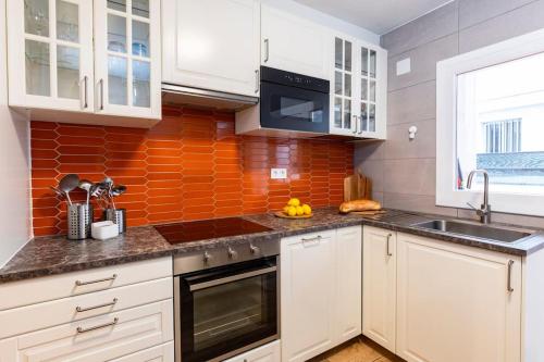 a kitchen with white cabinets and an orange wall at Casa Coli in Sabiñánigo