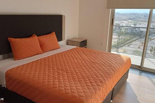 a bedroom with a bed with an orange comforter and a window at Departamento nuevo en High Towers Elite, Sonata in Lomas de Angelopolis