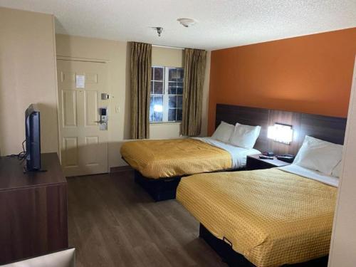 a hotel room with two beds and a television at Suburban Studios Winston-Salem near Hanes Mall in Winston-Salem