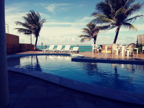 a swimming pool with chairs and palm trees and the ocean at Atlântico Flat in Natal