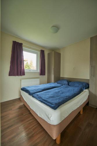 a bedroom with a bed with blue sheets and a window at Chalet de Elina - comfortable chalet for a relaxing stay in Voorthuizen